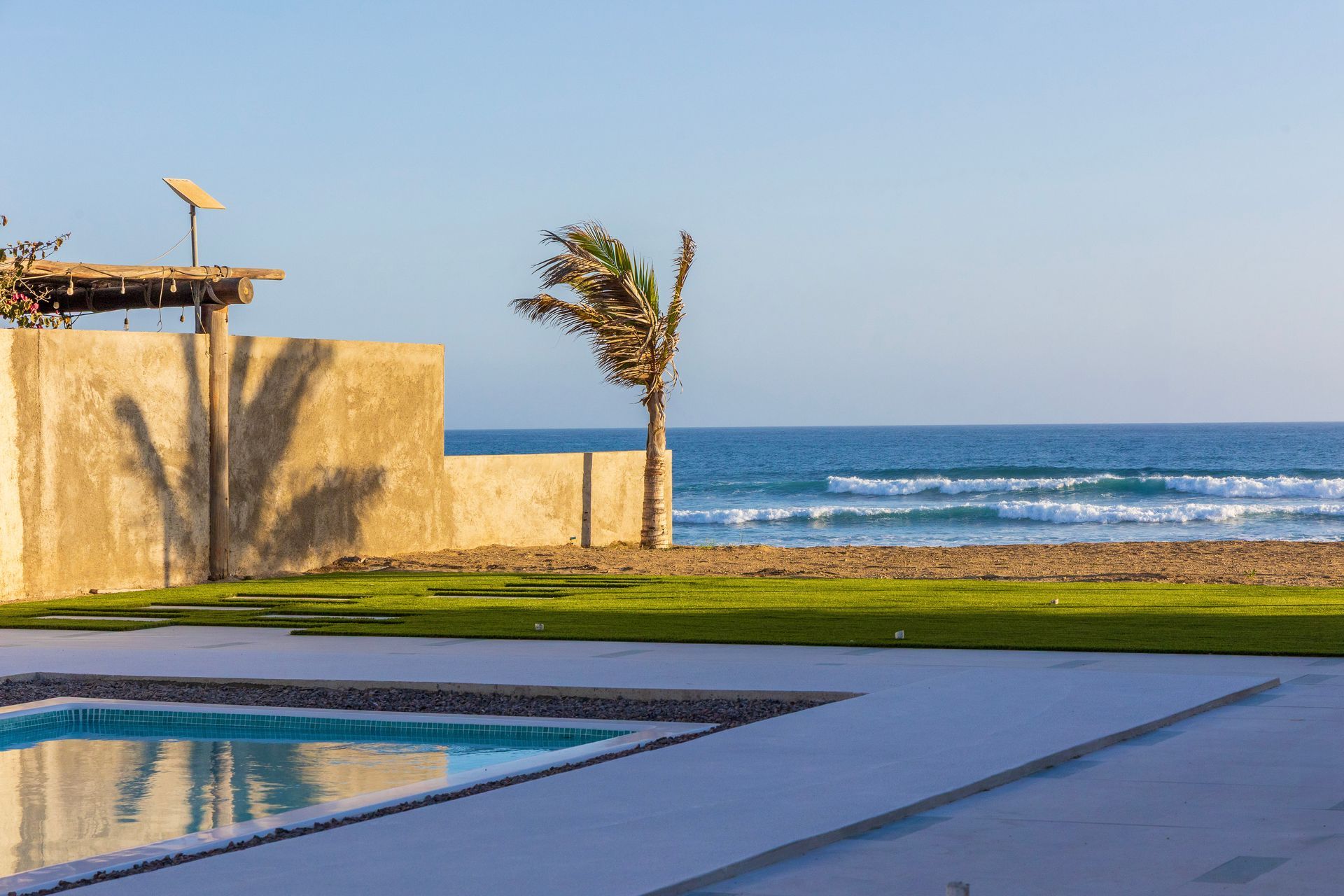 Oceanfront property with pool, palm tree, concrete wall, and blue sky.