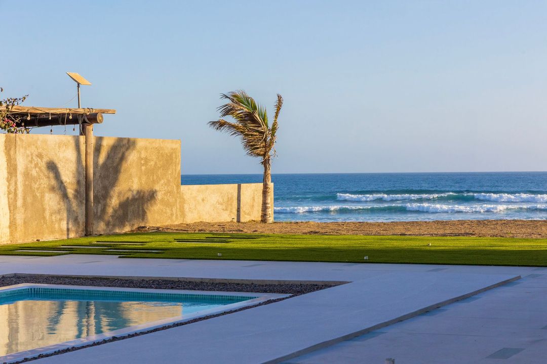 Oceanfront property with pool, palm tree, concrete wall, and blue sky.