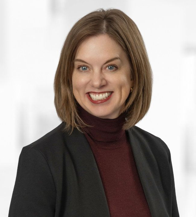 A woman in a black jacket is smiling for the camera.