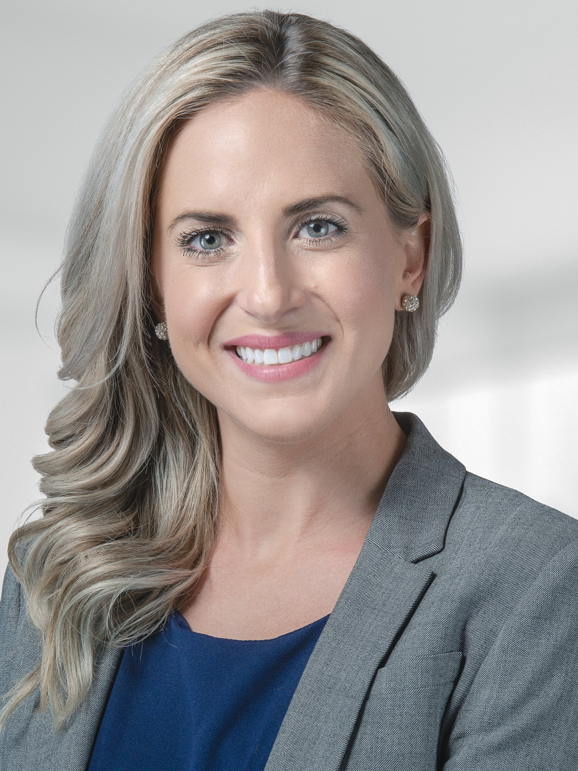 A woman wearing a gray jacket and a blue shirt is smiling for the camera.