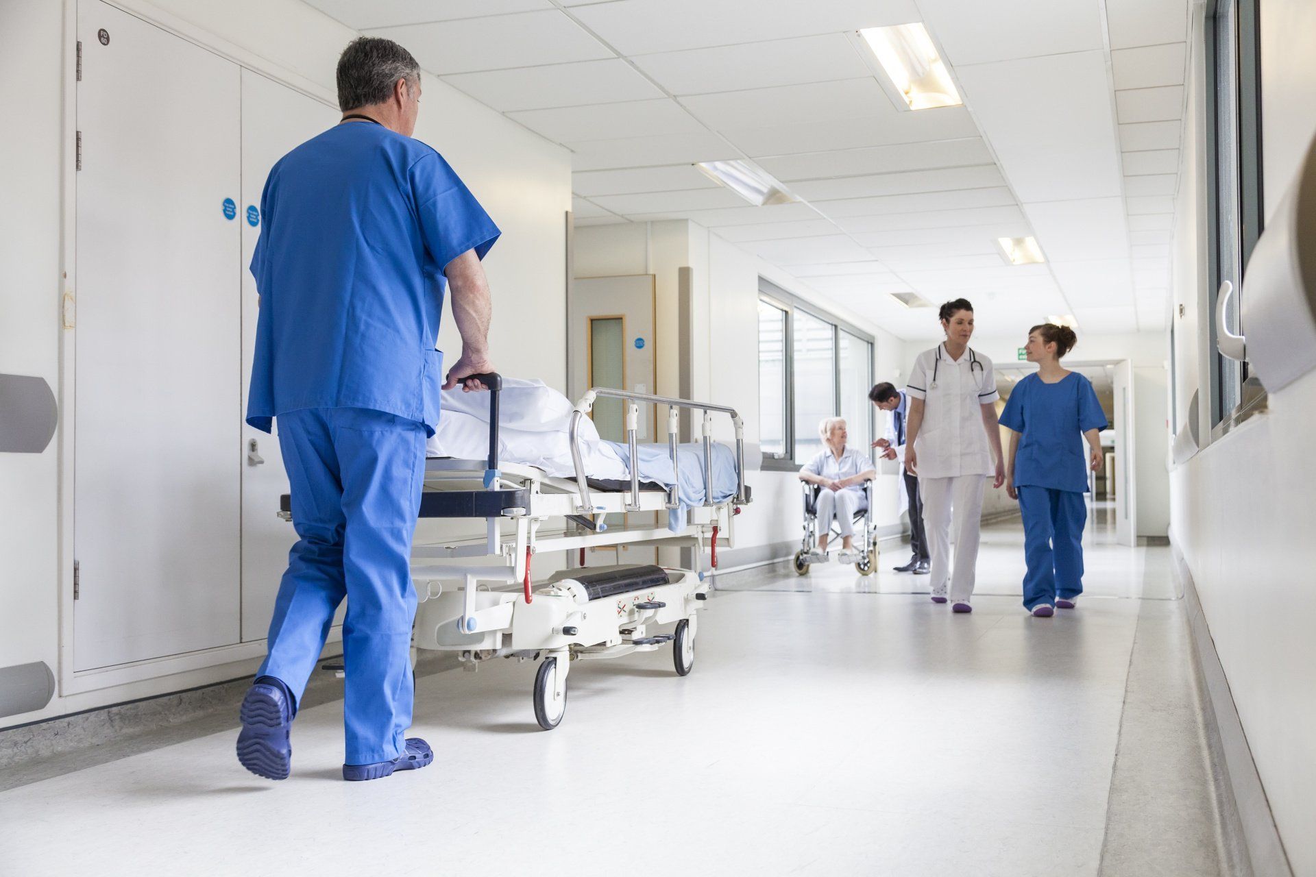 A nurse is pushing a hospital bed down a hospital hallway.