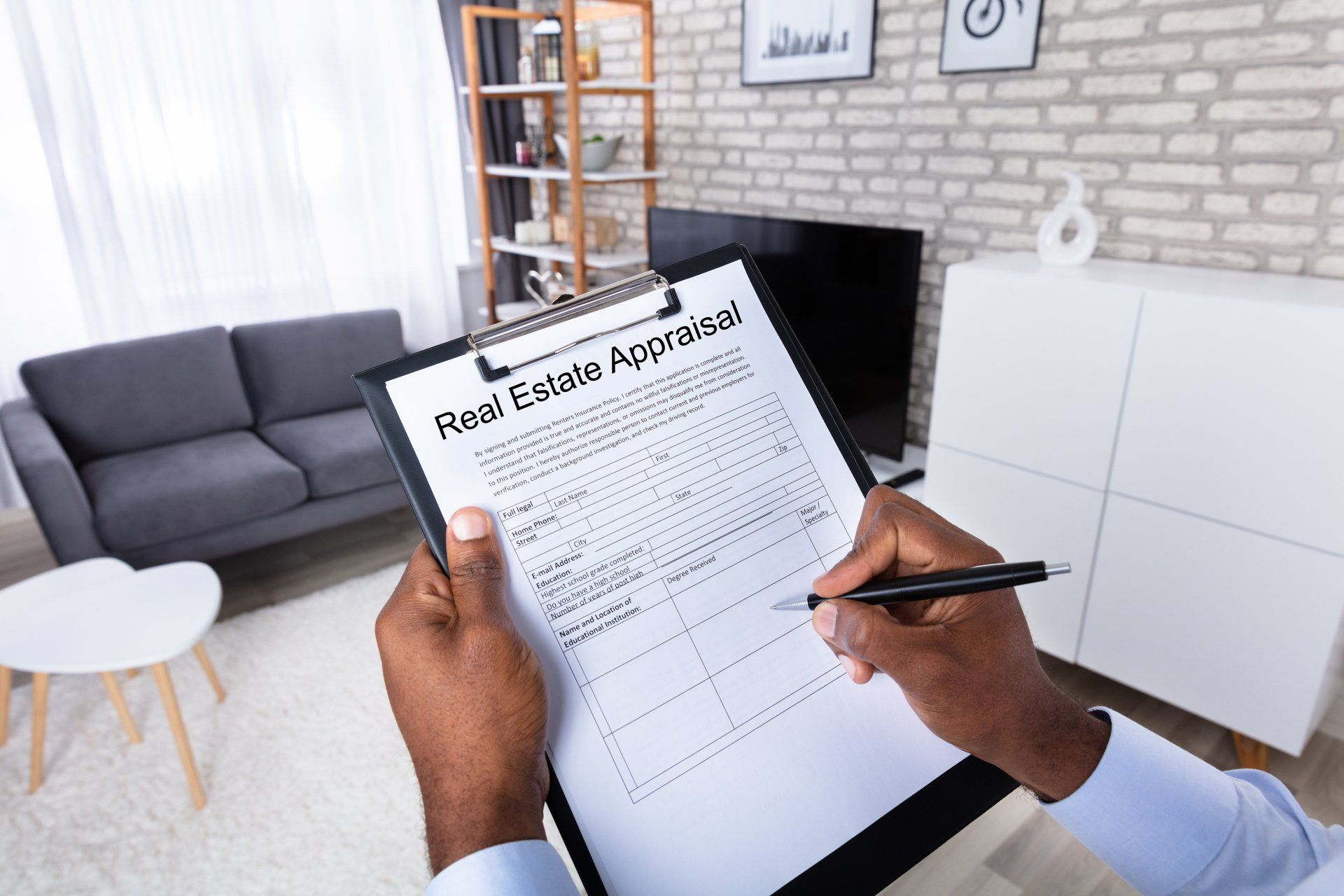 A man is signing a real estate appraisal on a clipboard in a living room.