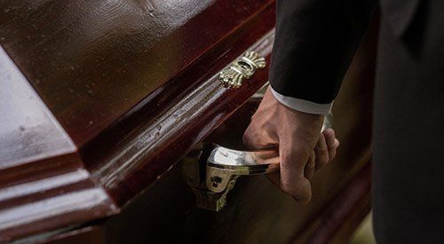 A man in a suit is opening a coffin with his hand.