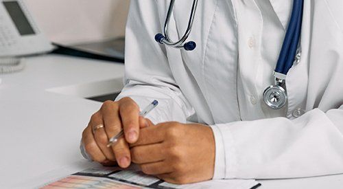 A doctor is sitting at a desk writing on a piece of paper.