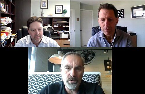 Three men are sitting in front of a computer screen.