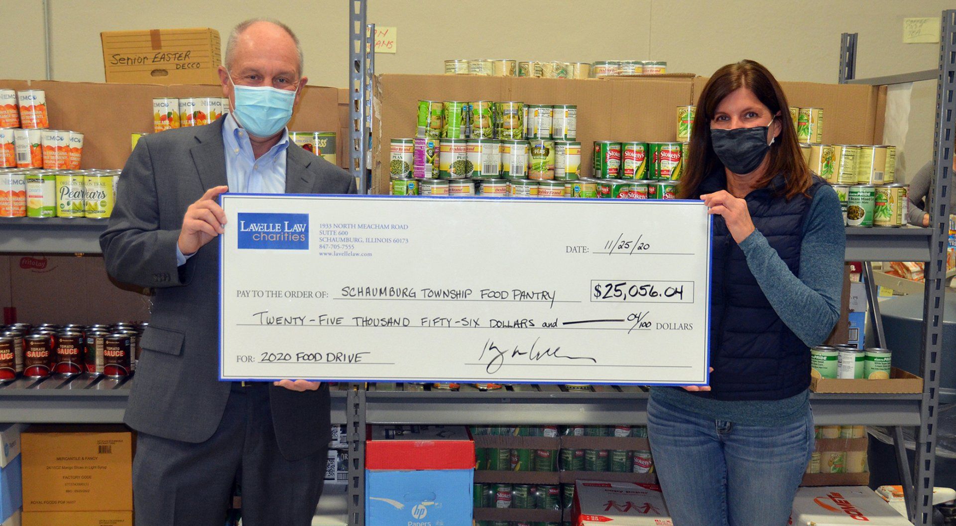 A man and a woman wearing masks are holding a large check.