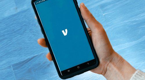 A person is holding a cell phone with the letter v on the screen.