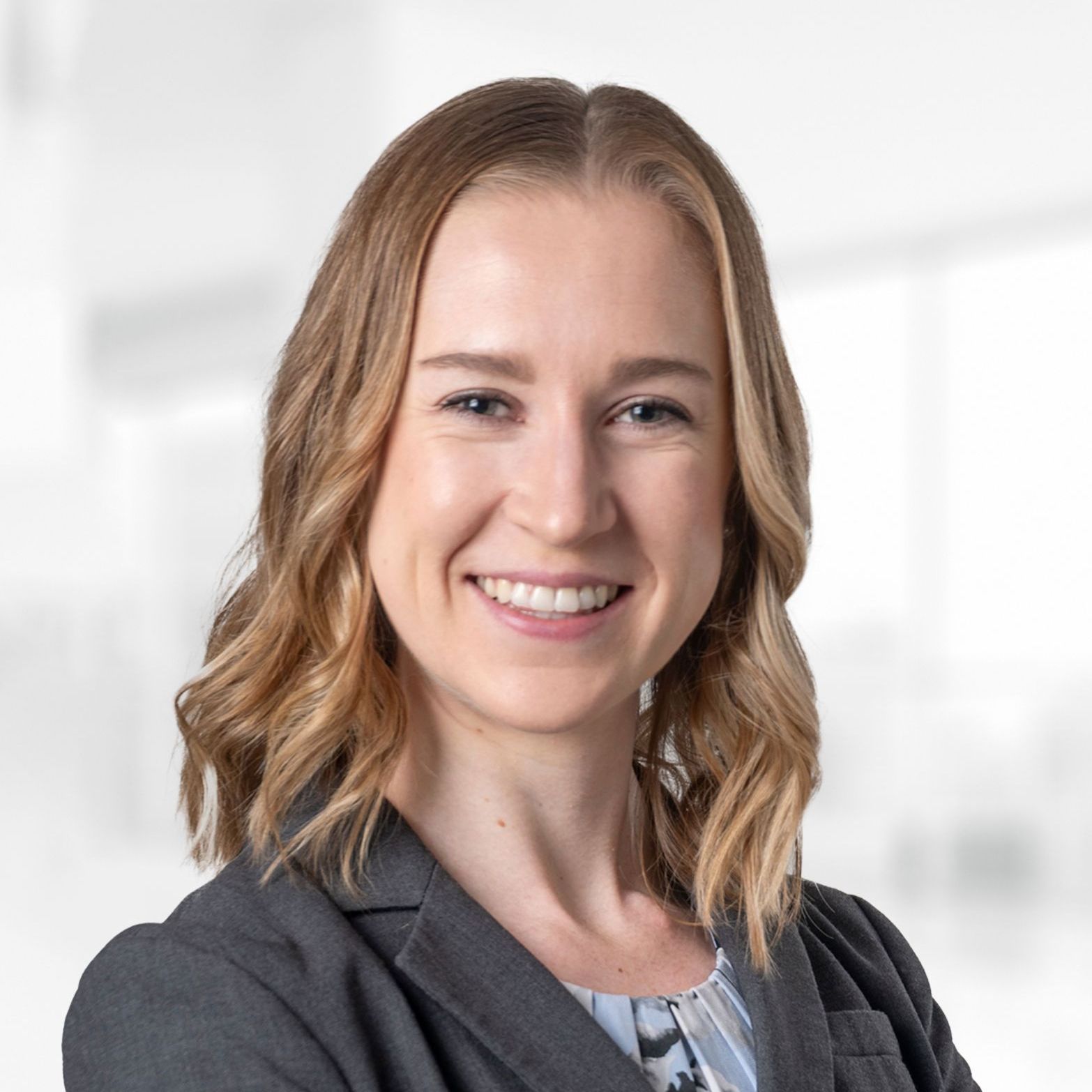 A woman in a suit is smiling for the camera with her arms crossed.
