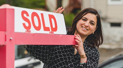 A woman is holding a sold sign in front of a house.