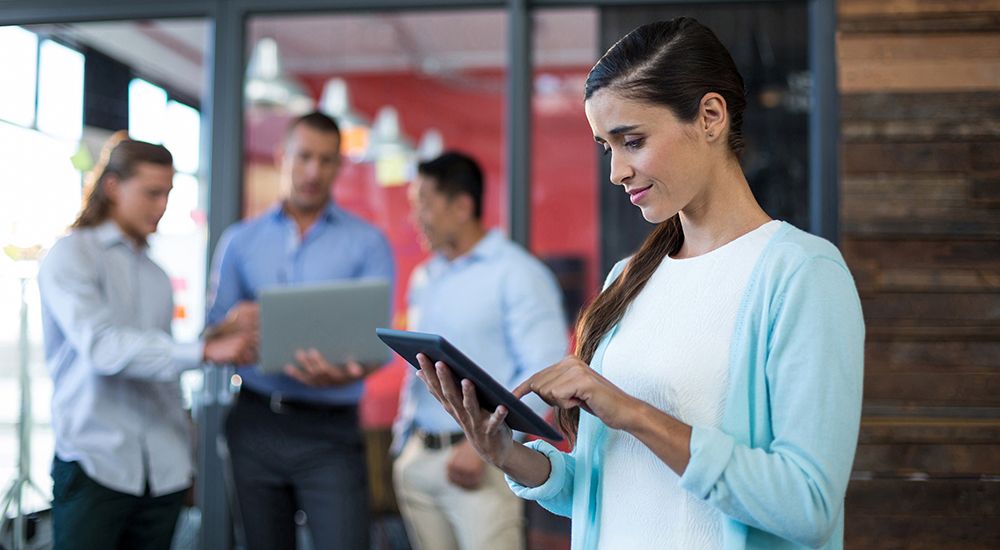 A woman is using a tablet computer while standing in front of a group of people.