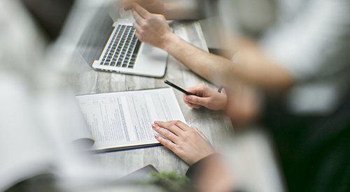 A group of people are sitting at a table with a laptop and papers.