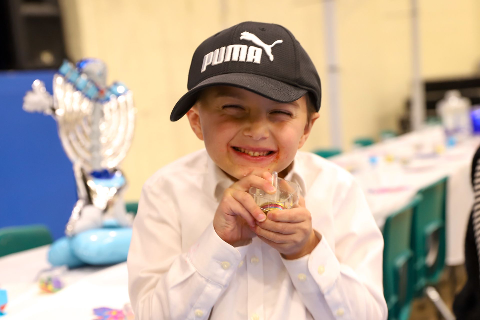 A young boy wearing a puma hat is posing for a picture with a dreidel.