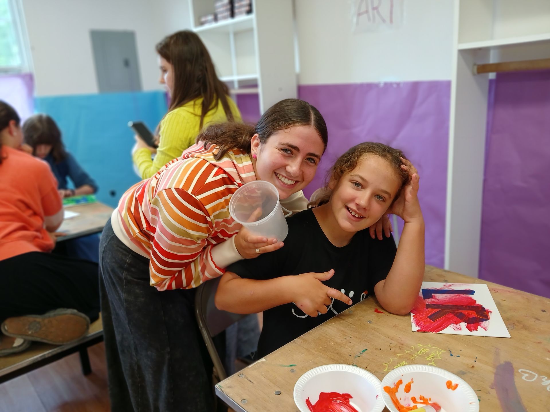 Two girls are posing for a picture while sitting at a table.