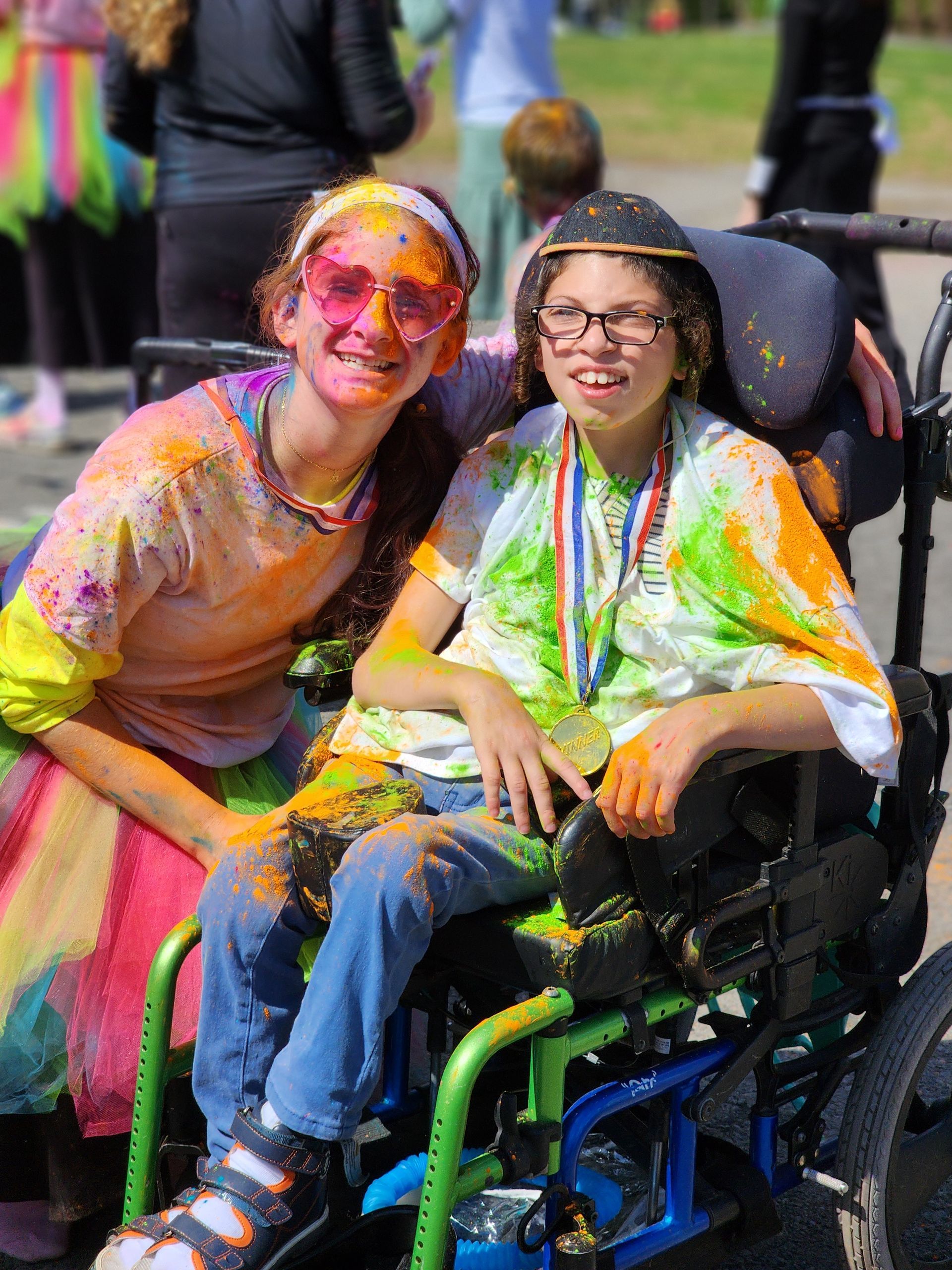 A girl is sitting next to a young boy in a wheelchair covered in powder paint.