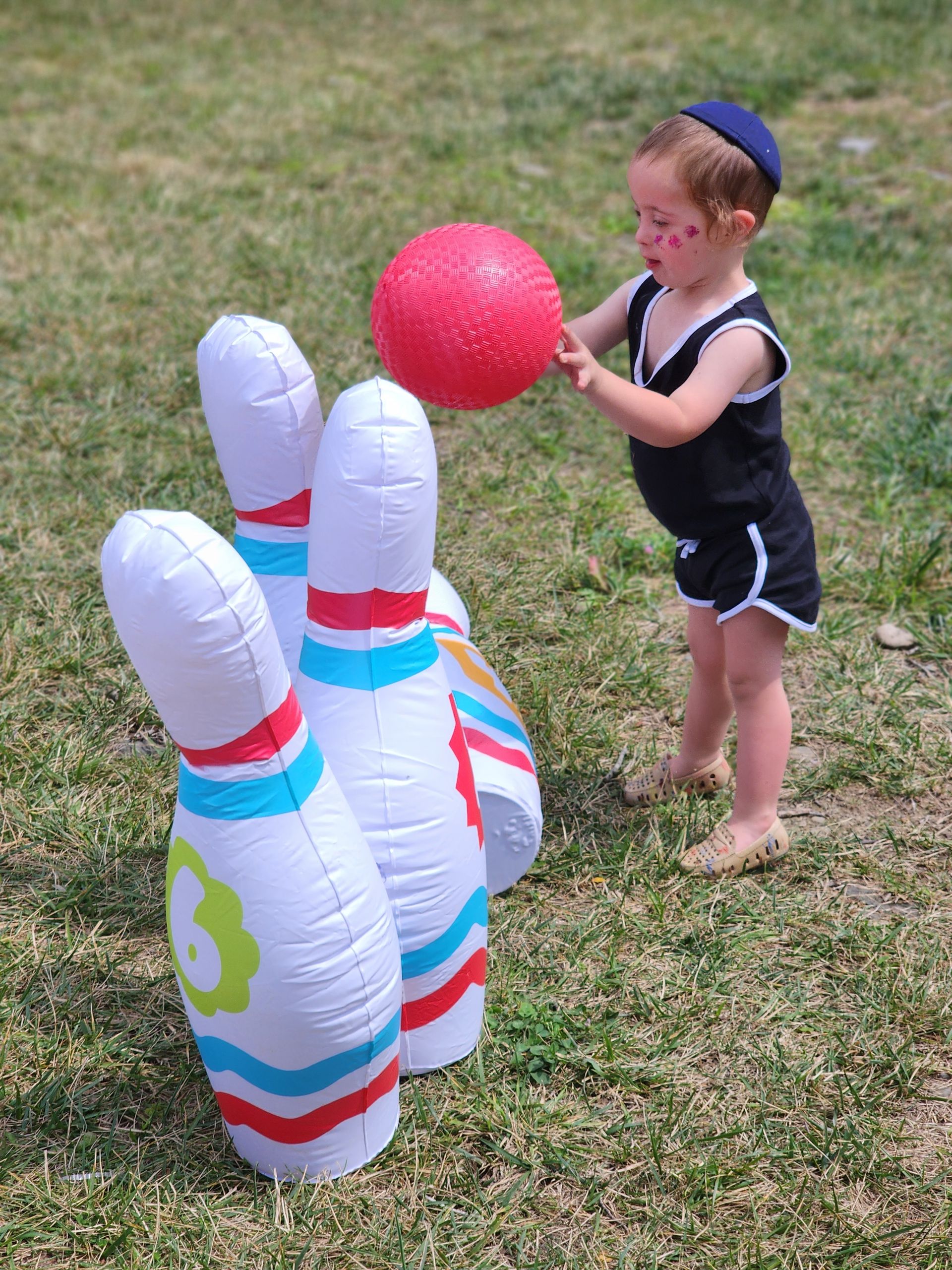 A little boy is playing with an inflatable bowling set.