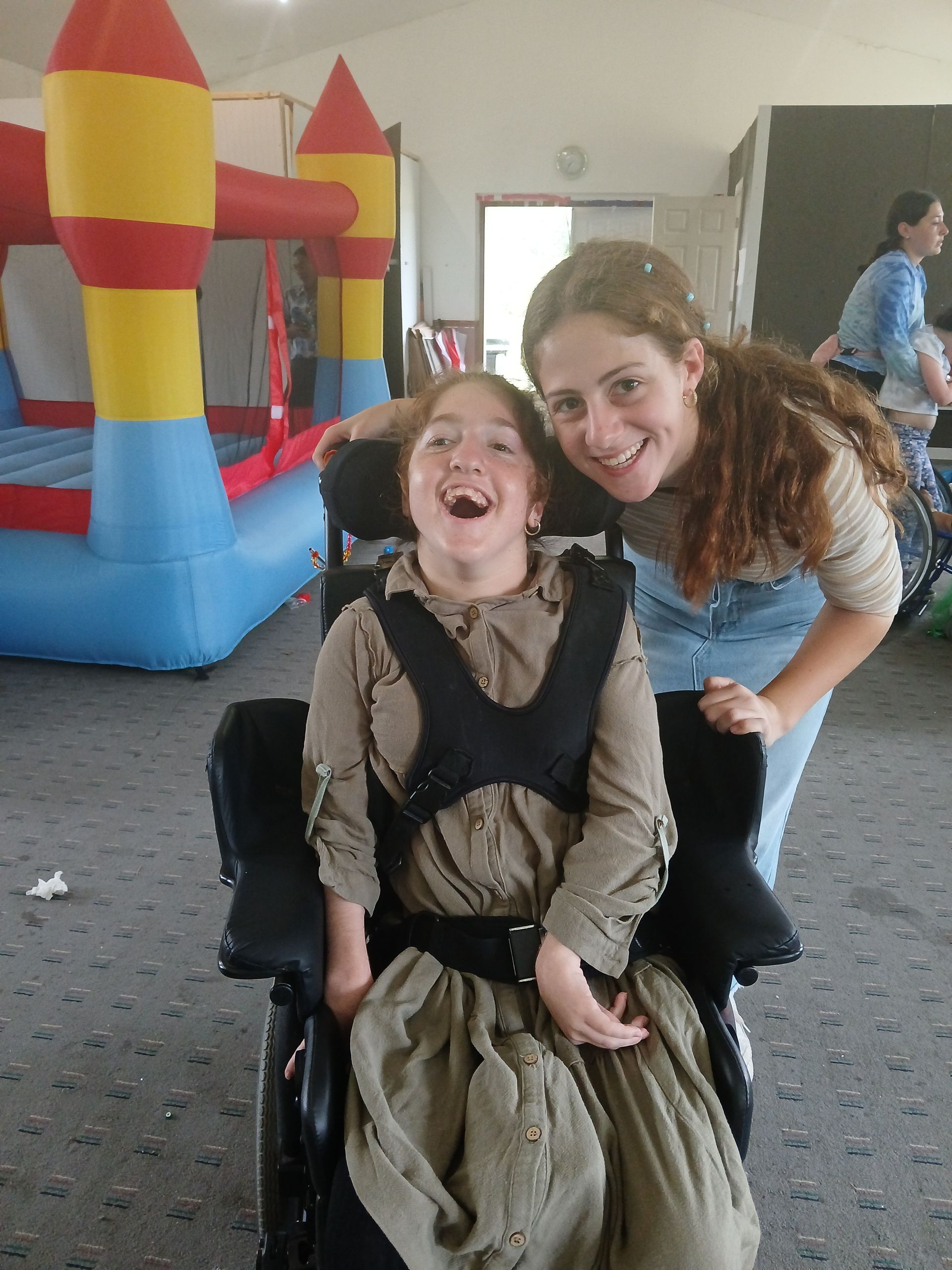 A woman is standing next to a girl in a wheelchair in front of a bouncy house.