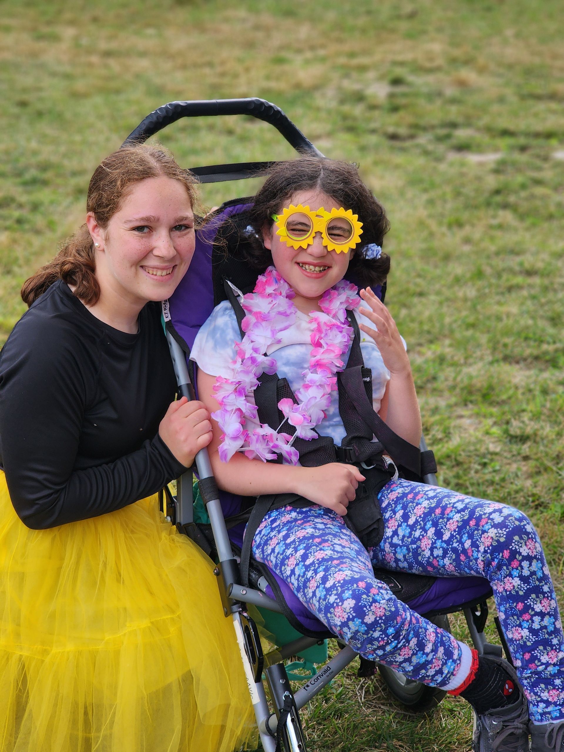 A girl in a yellow skirt is sitting next to a girl in a wheelchair.