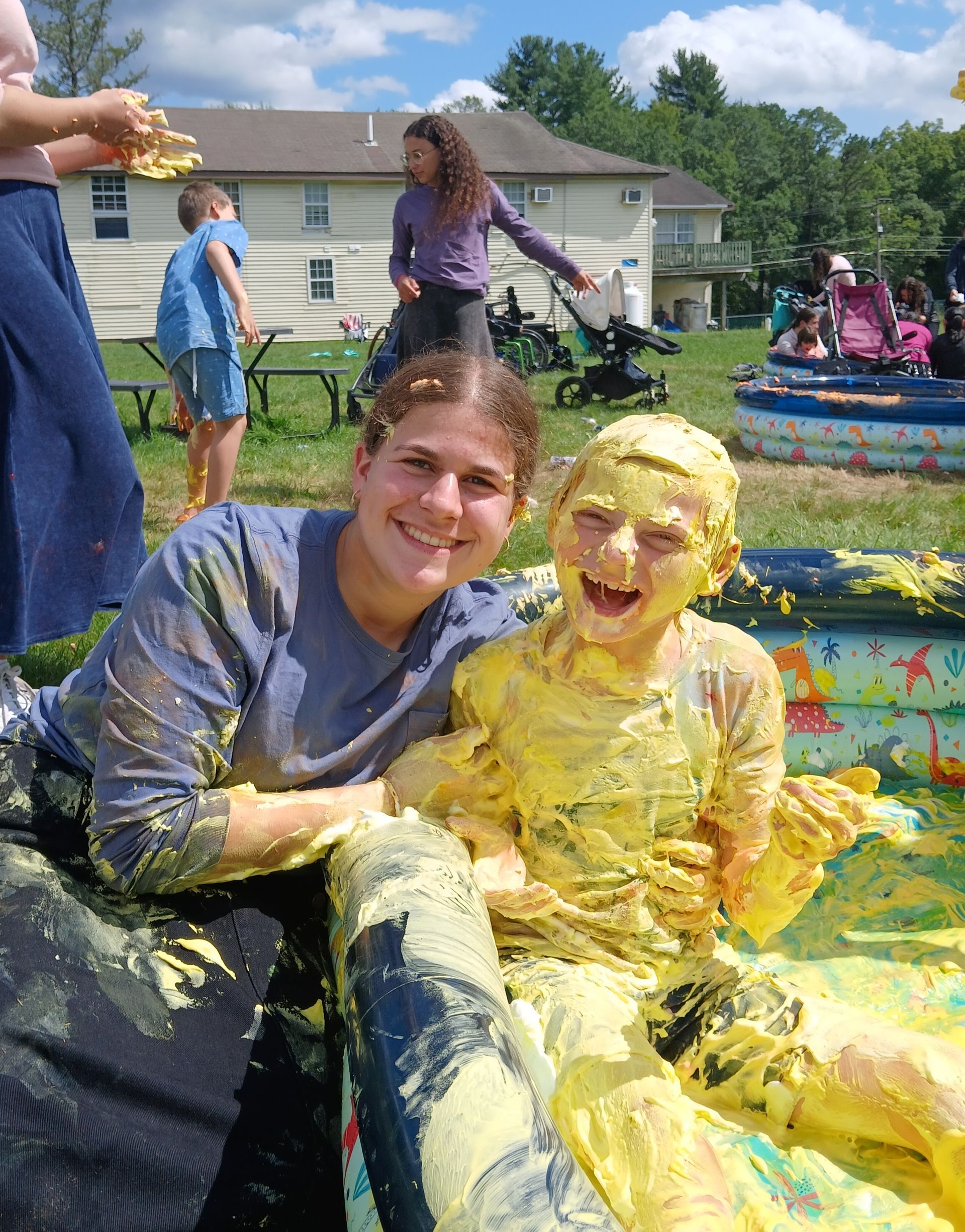 A girl and a child are covered in yellow painted shaving cream.