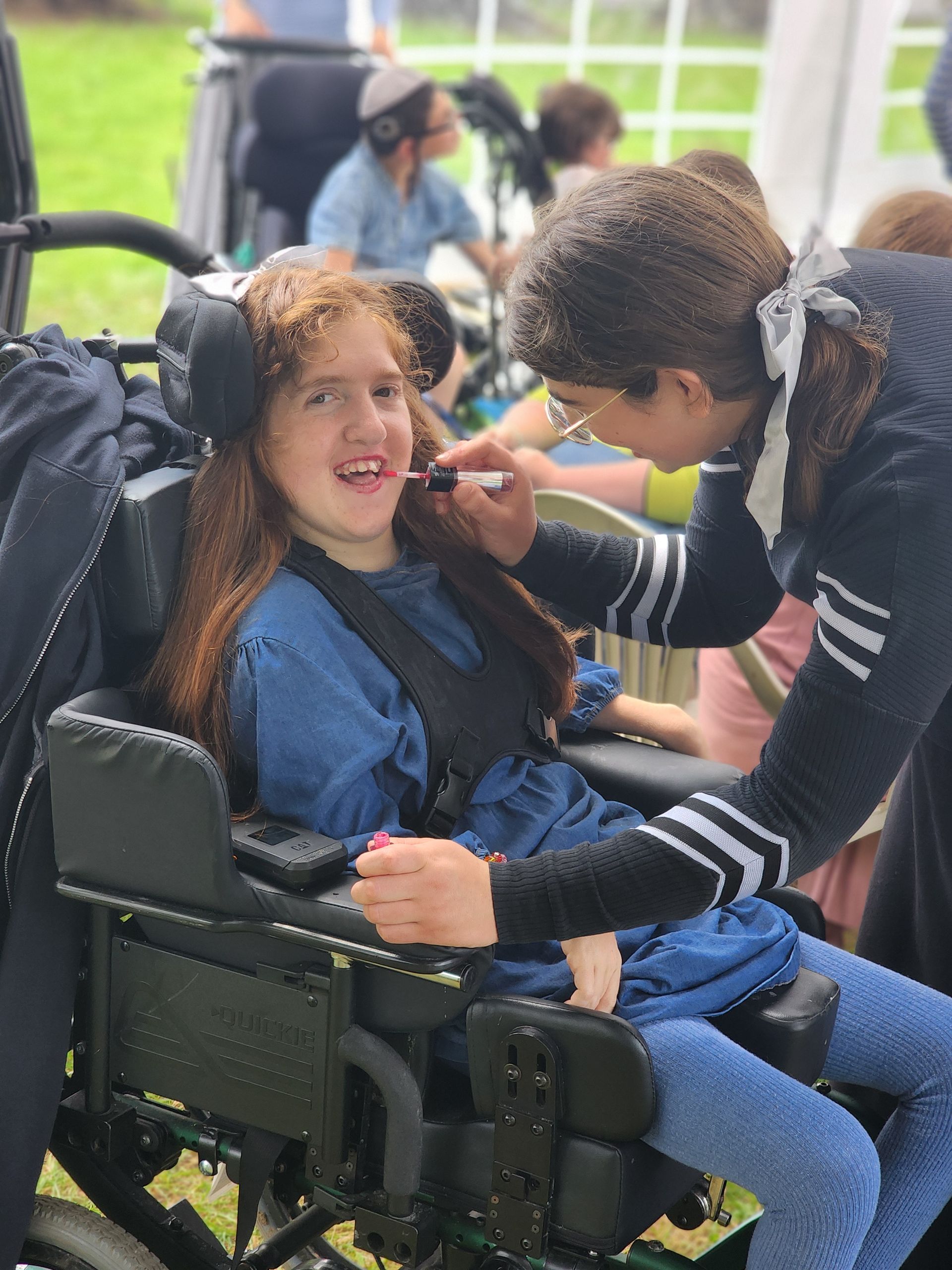 A woman is applying makeup to a young girl in a wheelchair.
