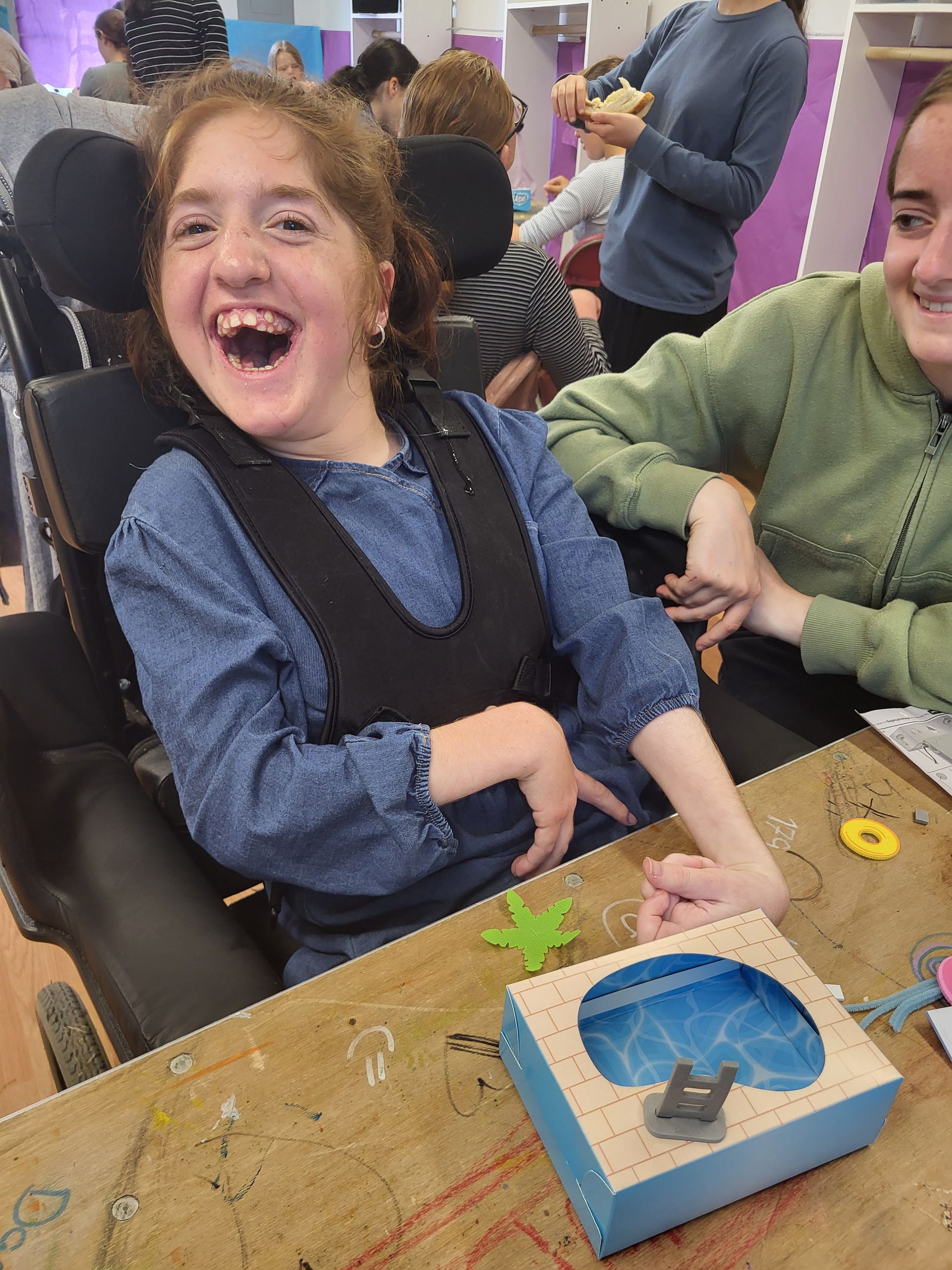 A girl in a wheelchair is sitting at a table laughing.