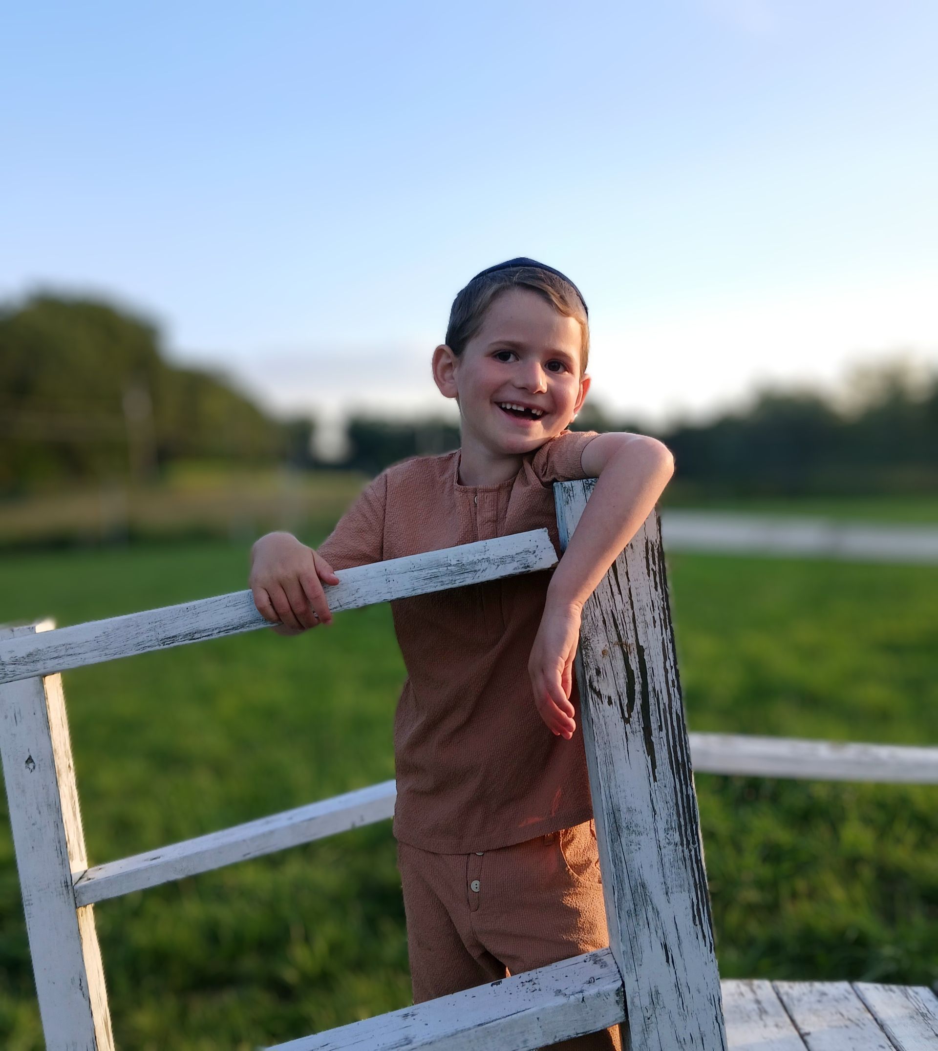 A young boy leaning against a white fence in a field