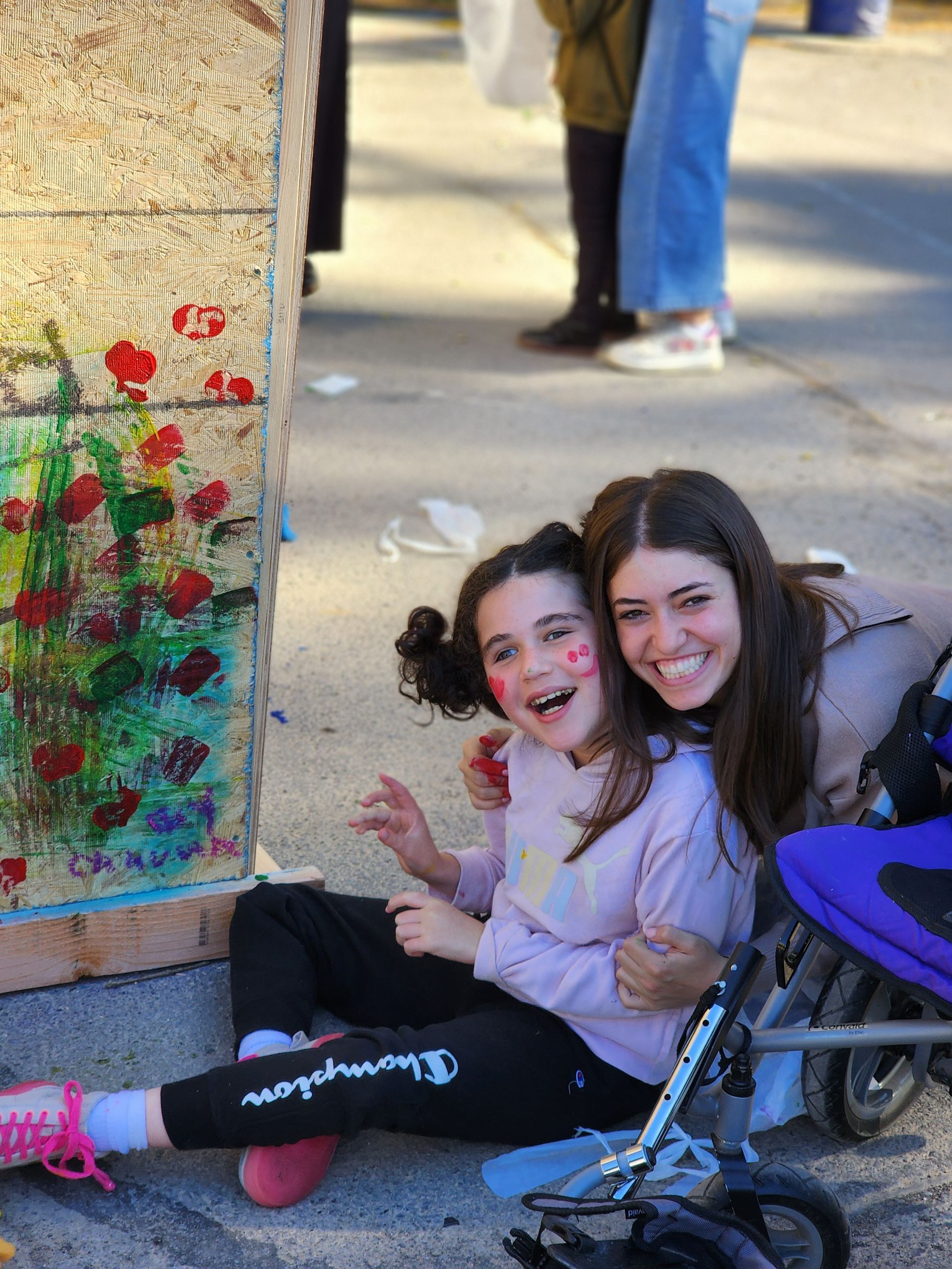 Two girls are sitting on the ground next to a stroller.