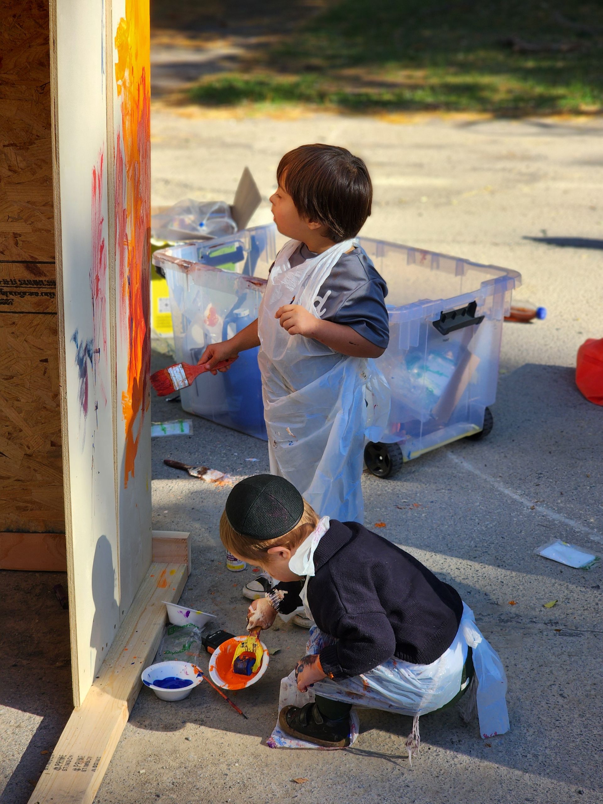 Two young boys are painting a wall outside.
