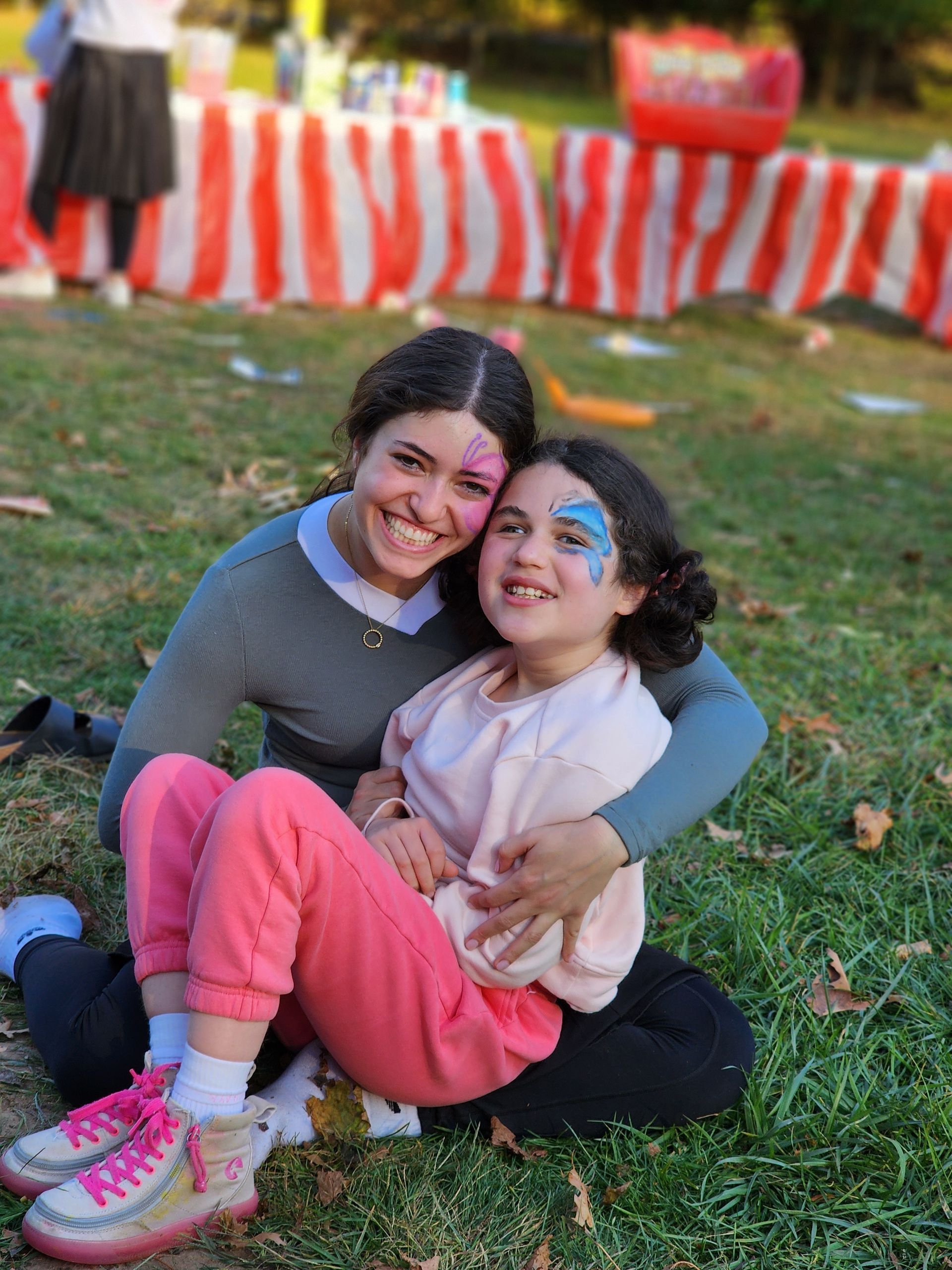 A woman and a little girl are sitting on the grass with their faces painted.