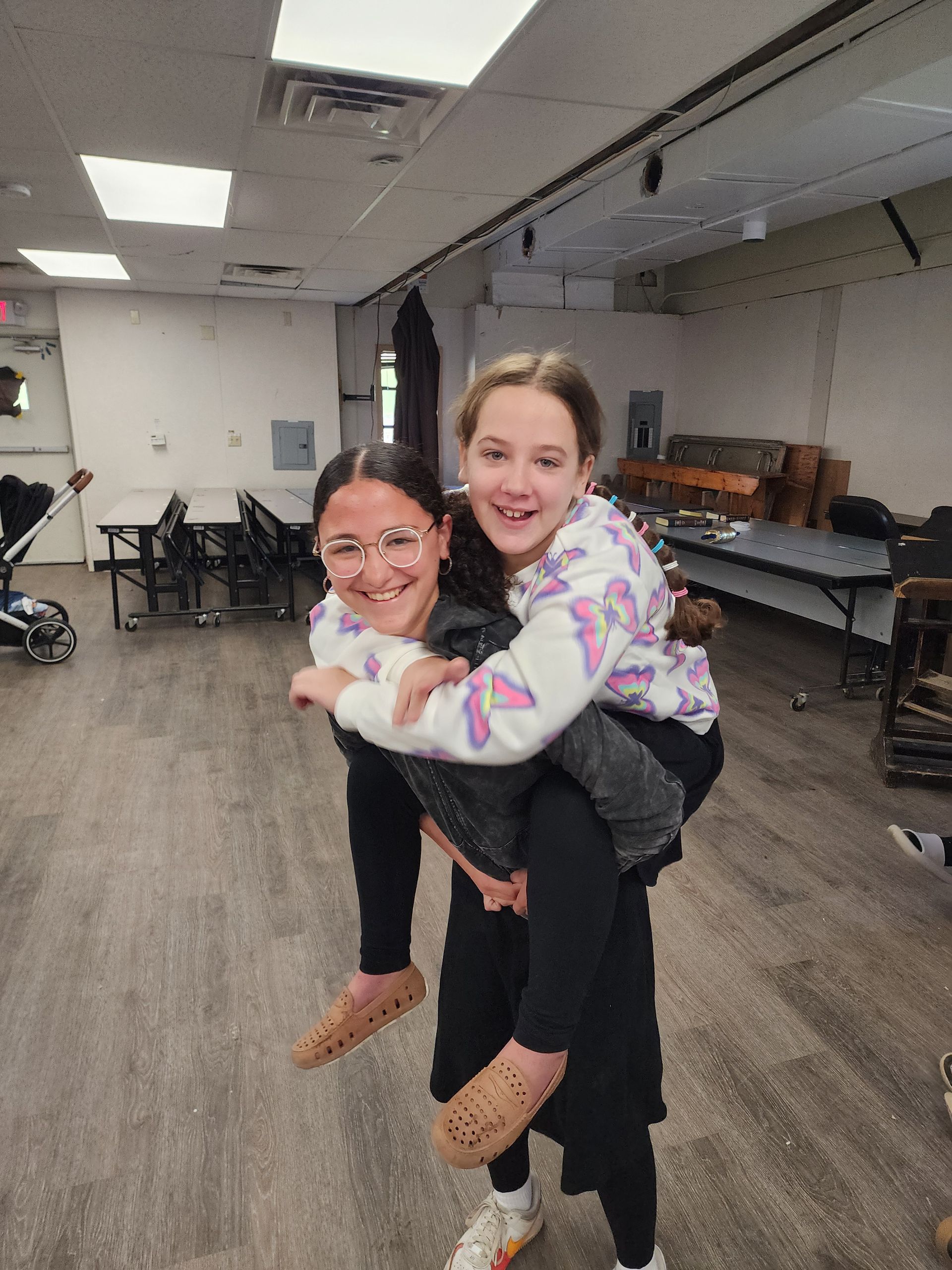 A girl is carrying another girl on her back in a room.