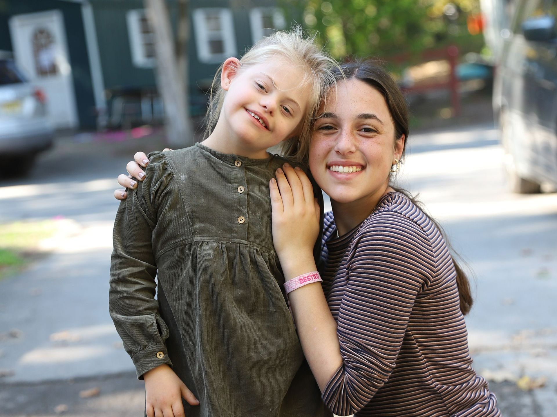 Two girls are posing for a picture together on the sidewalk.