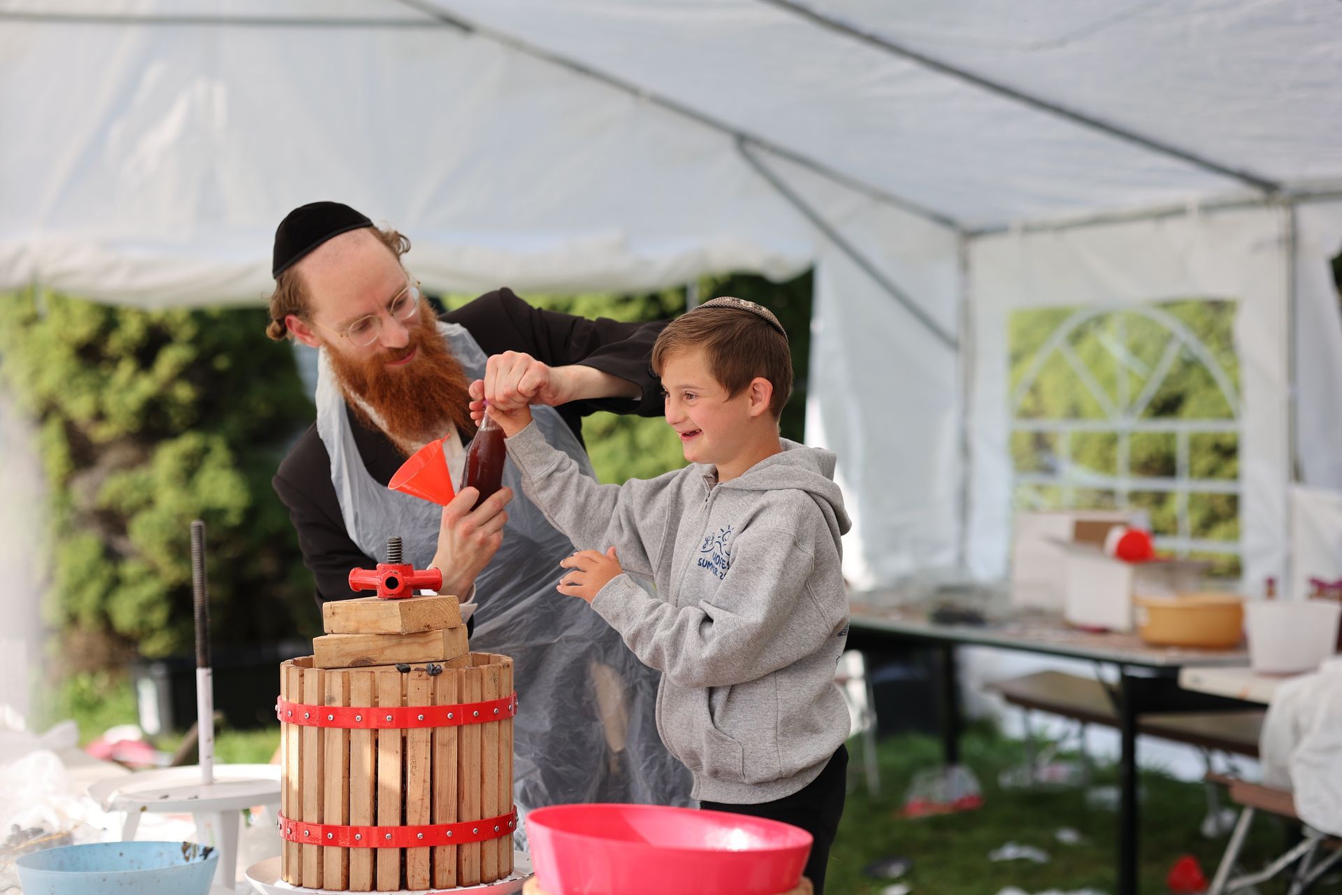 A man and a boy are making grape juice in a tent.