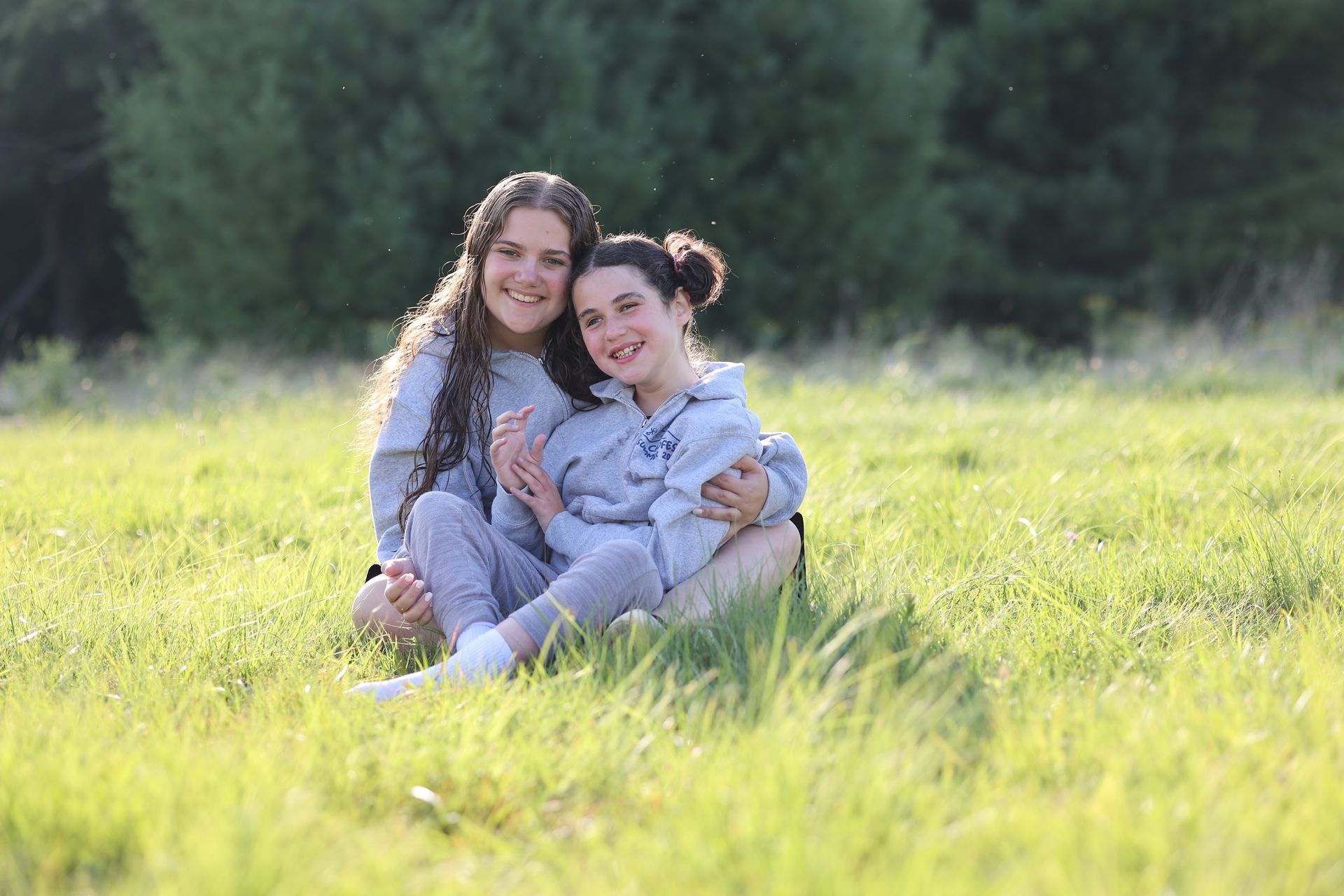 Two girls are sitting in the grass and smiling.