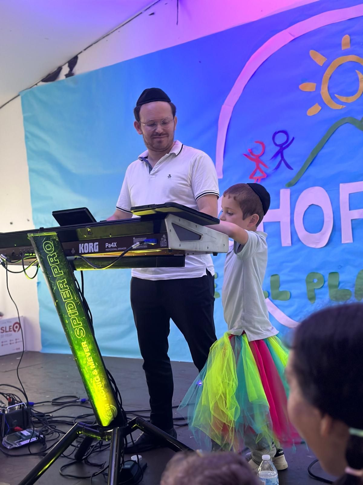 A man and a little girl are playing a keyboard in front of a sign that says hof
