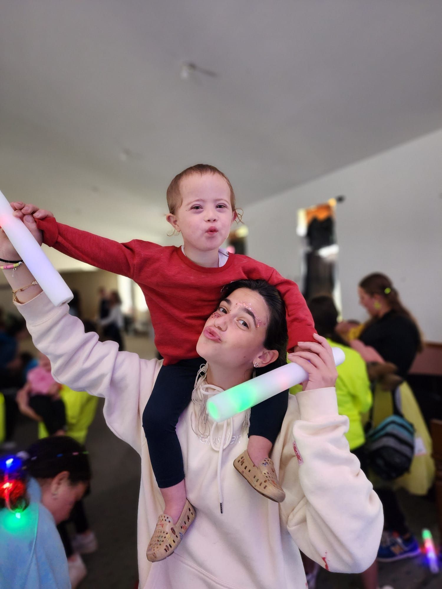 A woman is carrying a little boy on her shoulders while holding glow sticks.