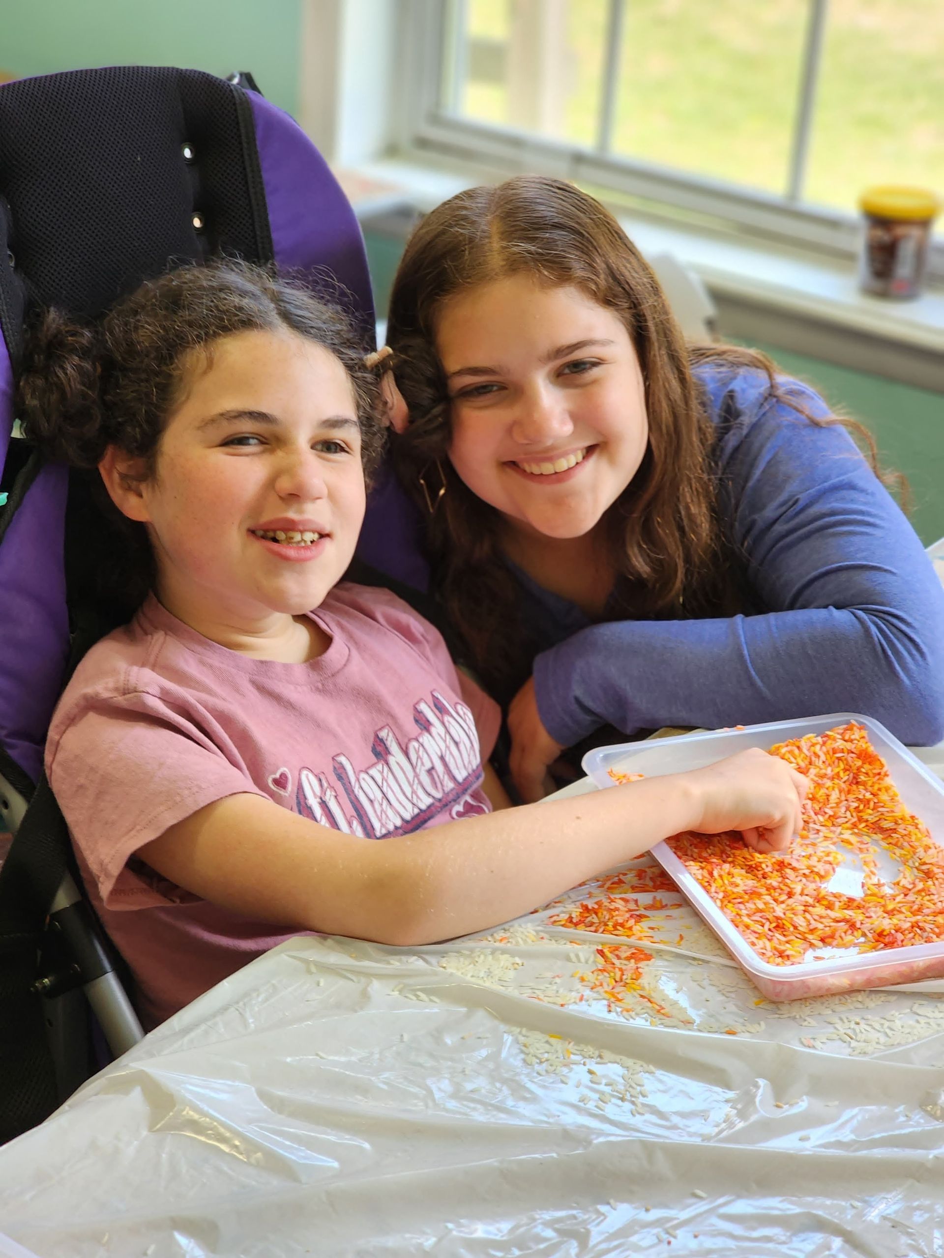 Two young girls are sitting at a table with a tray of food.