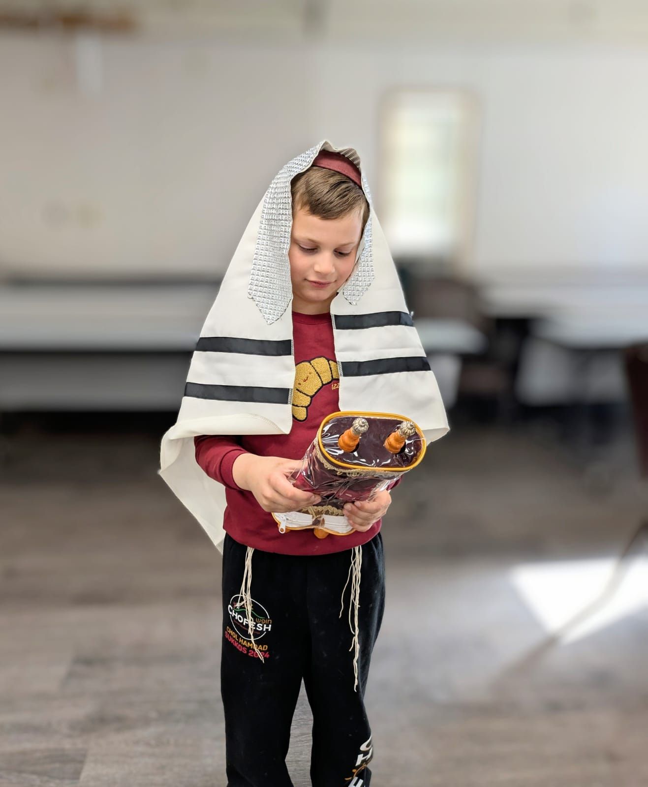 A young boy is wearing a tallit and holding a torah.
