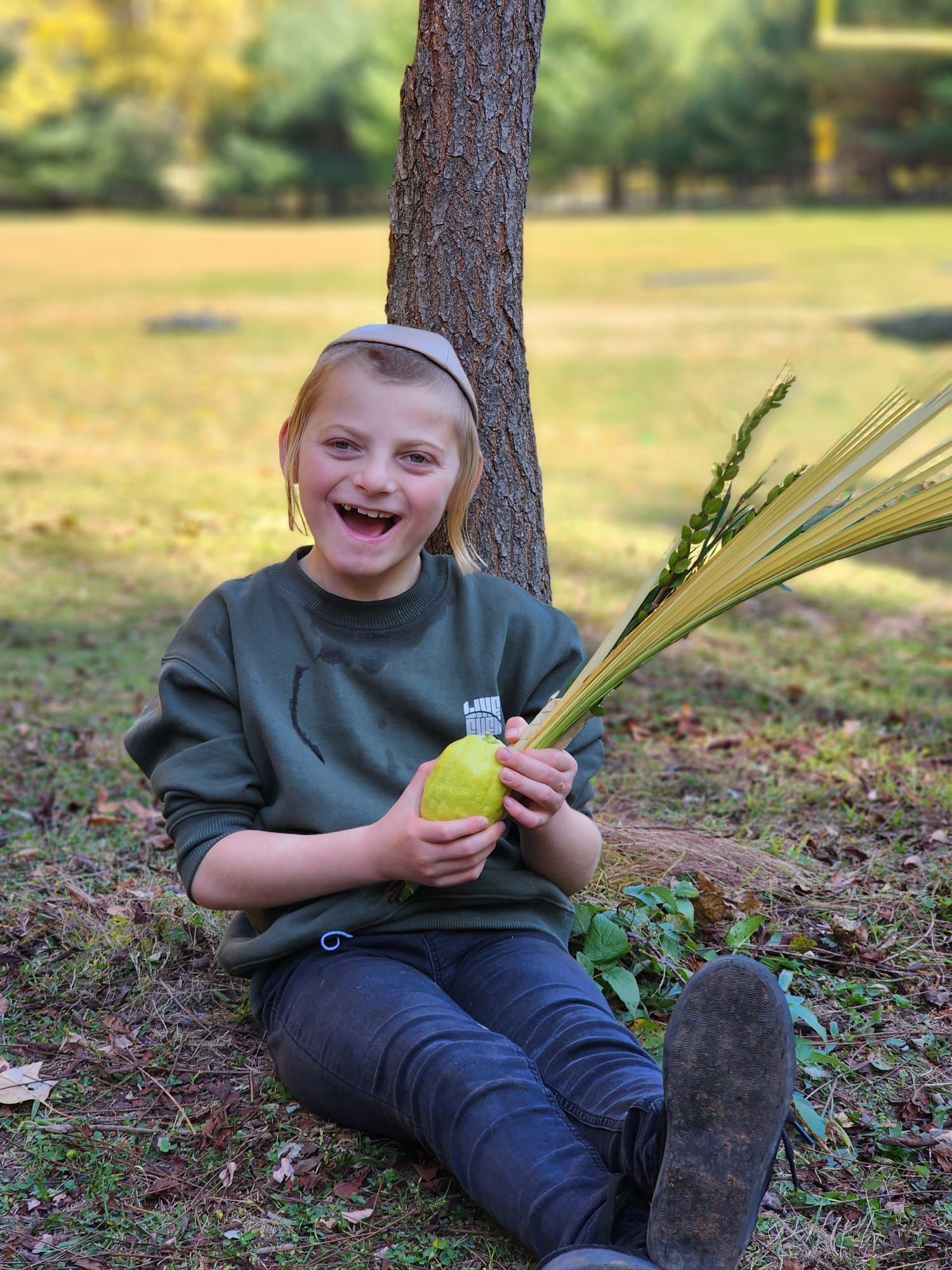 A young girl is sitting on the ground holding a pear and palm leaves.