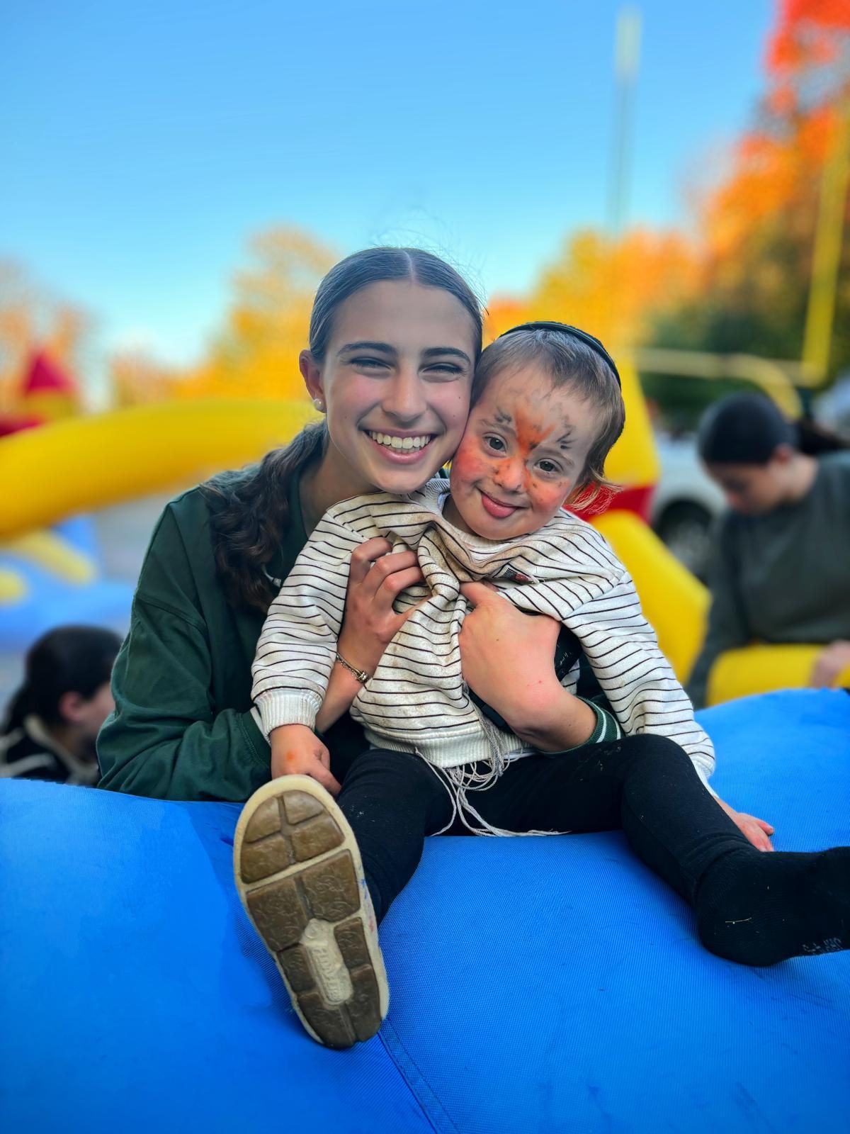 A teenage girl is holding a little boy with his face painted.