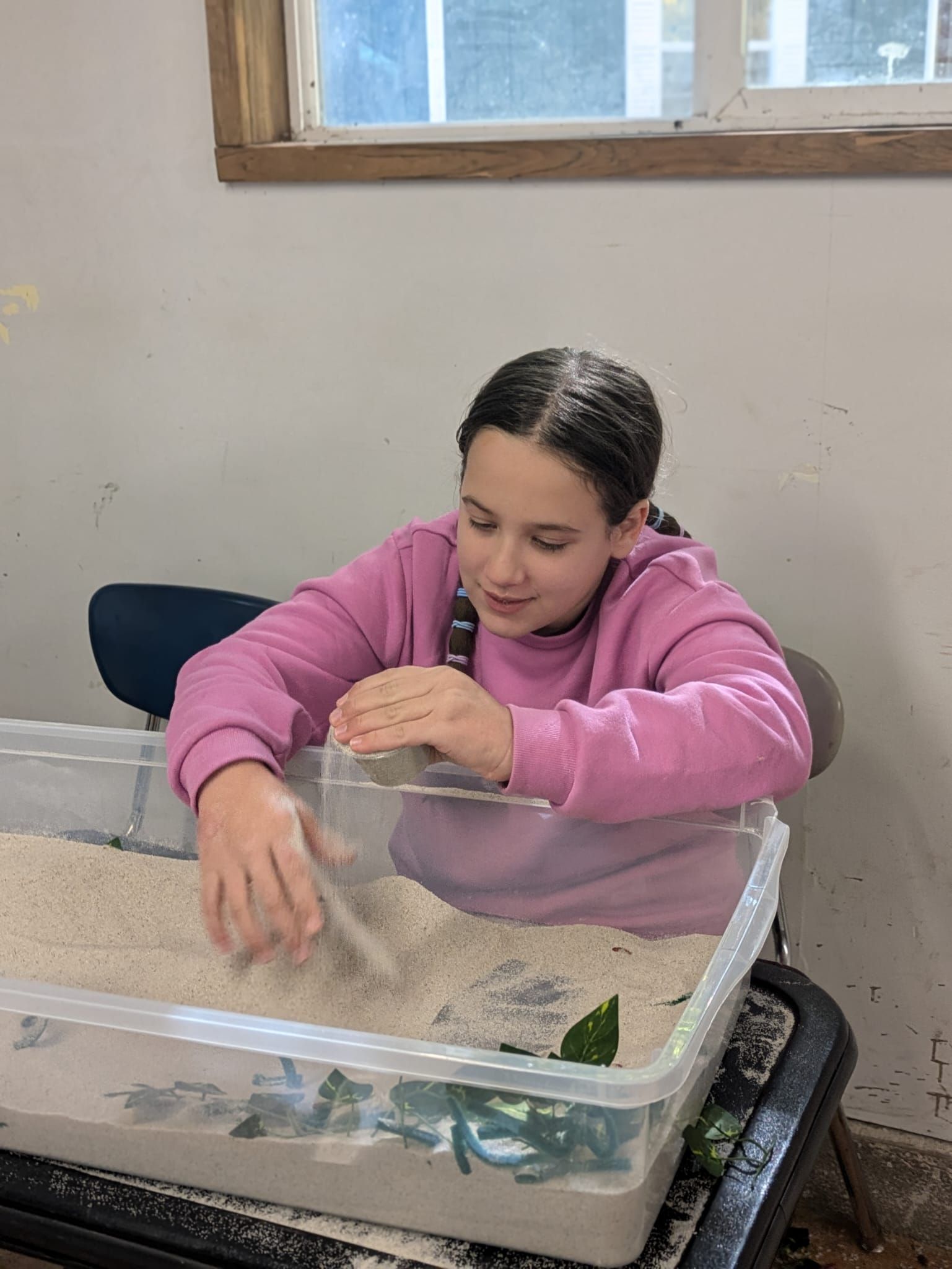 A young girl is playing with sand in a plastic container.