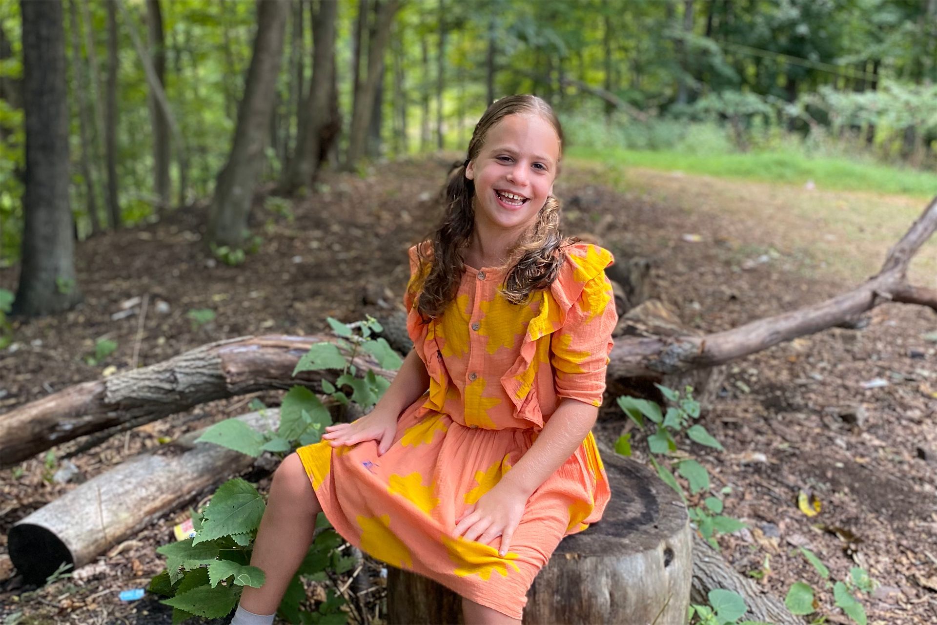 A young girl is sitting on a tree trunk and smiling.