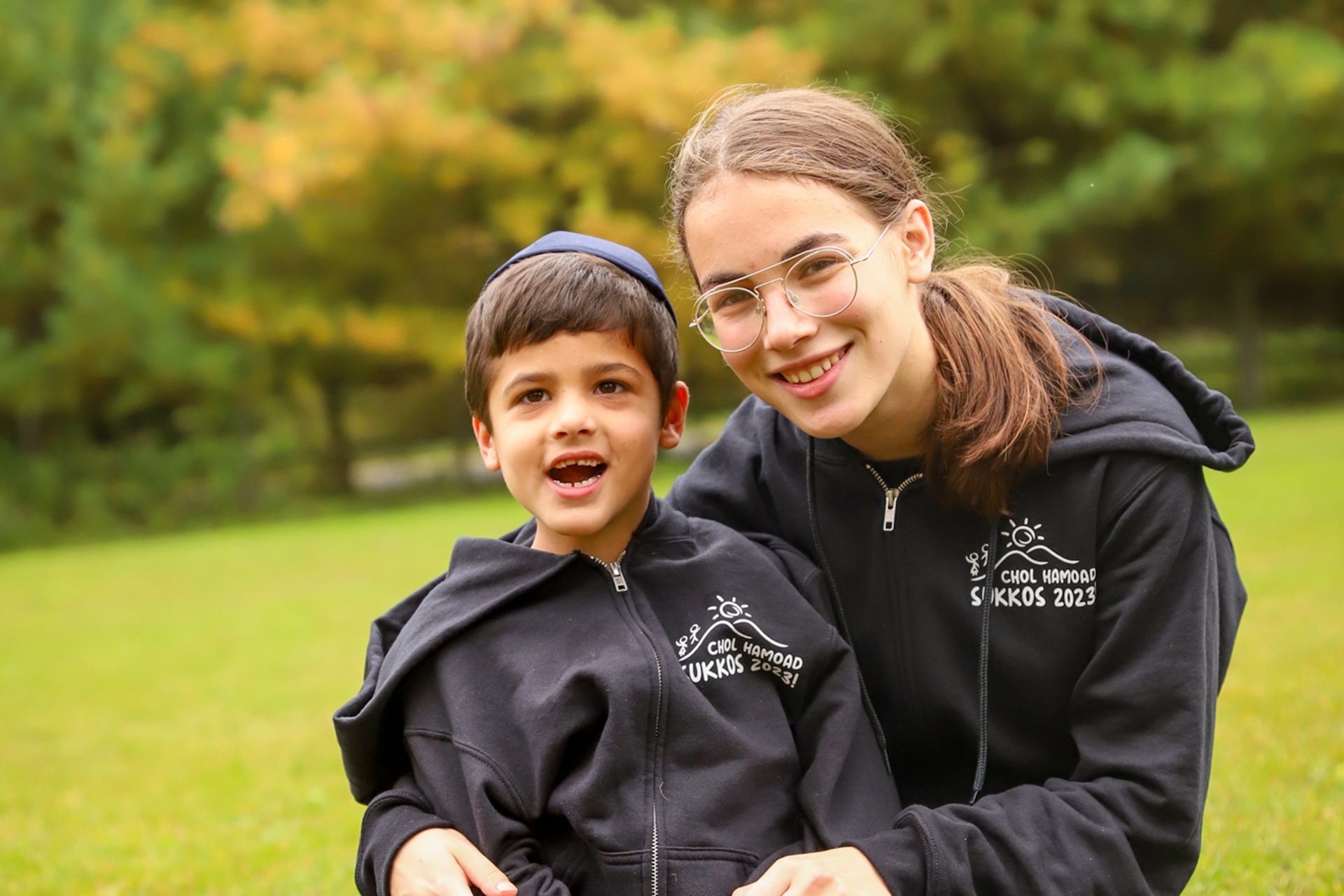 A girl and a young boy are posing for a picture in the grass.