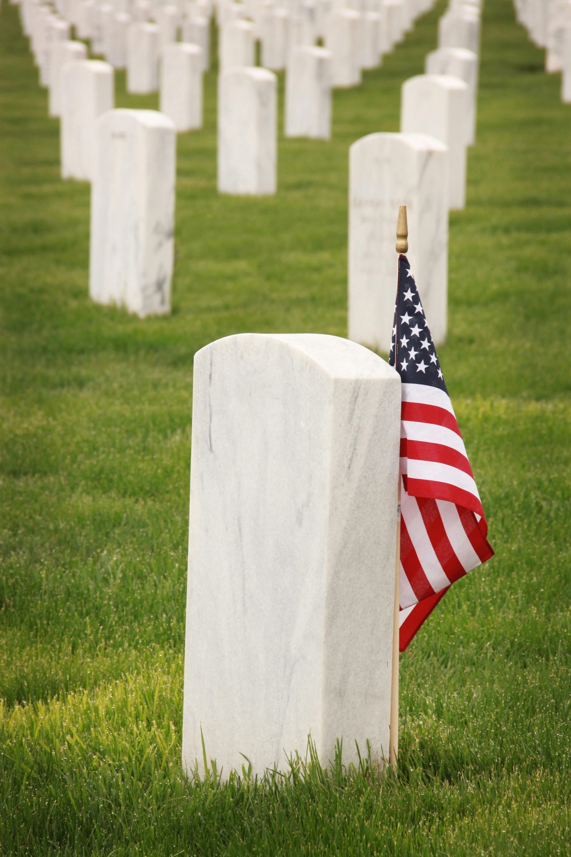 White gravestones in a cemetery, one marked with a small American flag.