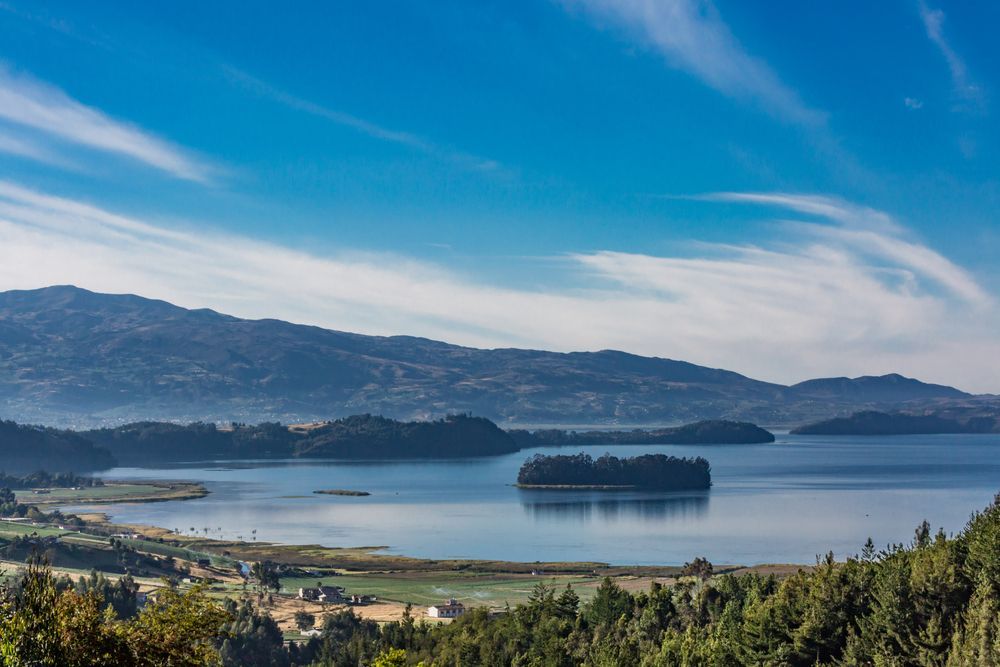 Lago rodeado de montañas y árboles bajo un cielo azul con nubes tenues.