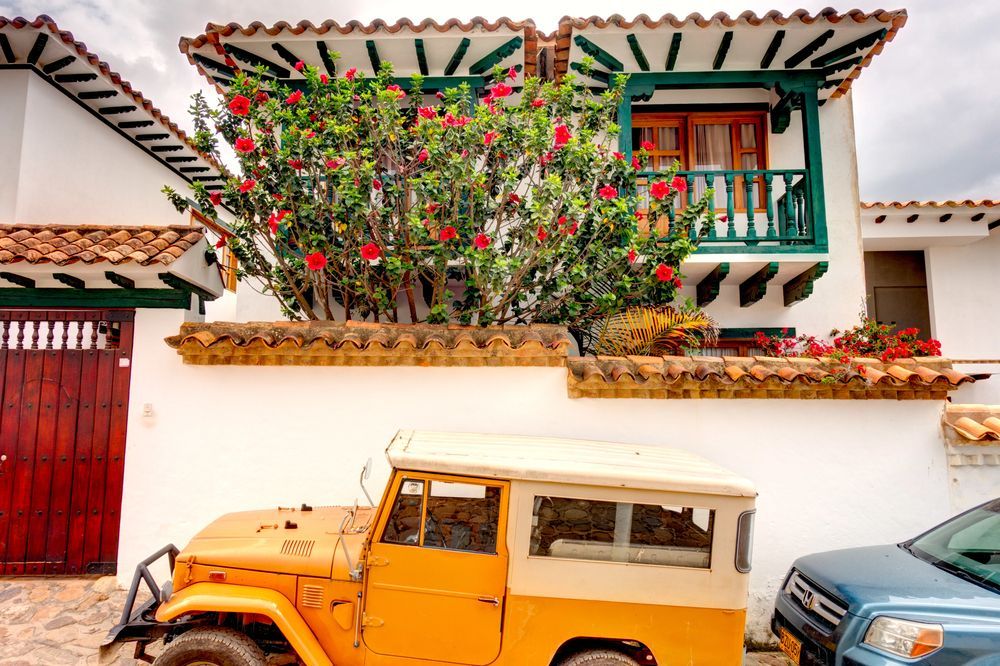 Jeep amarillo estacionado frente a un edificio blanco con balcón y flores rojas.
