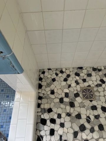 A shower with a black and white tile floor and a drain.