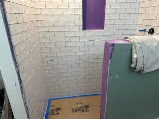 A bathroom with white tiles and a purple shower stall.