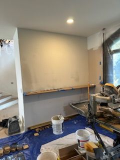 A room with a bucket of paint and a circular saw on the floor.