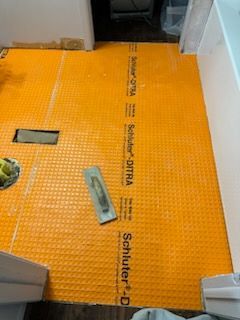 A bathroom floor with a yellow mat and a trowel on it.