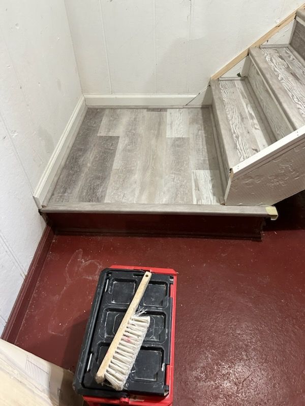 A broom and bucket are sitting on a red floor next to a set of stairs.