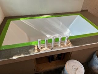 A bathroom sink with green tape around it is being painted.